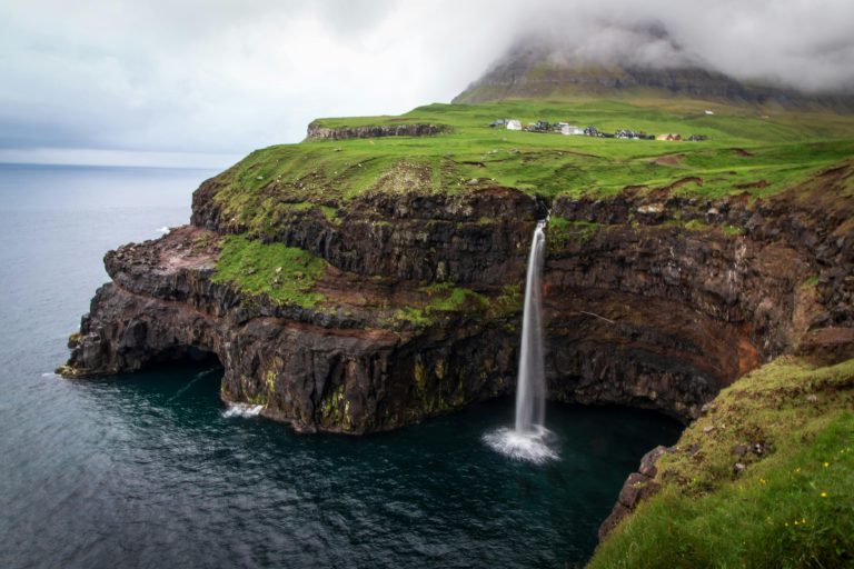 Discover the breathtaking waterfall flowing off a scenic cliff on the Faroe Islands, surrounded by lush greenery and serene ocean views.